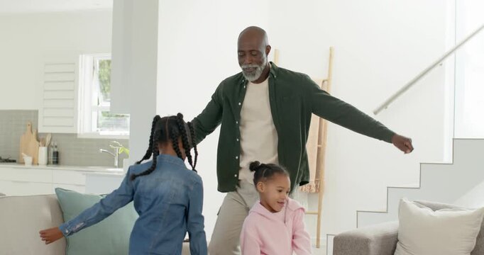 African American family dad opening arms urging denim jacket children dancing by ottoman at home