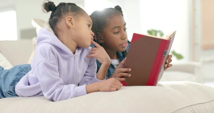 Two youth African American sisters lying on couch, reader holding book, reading, sharing story