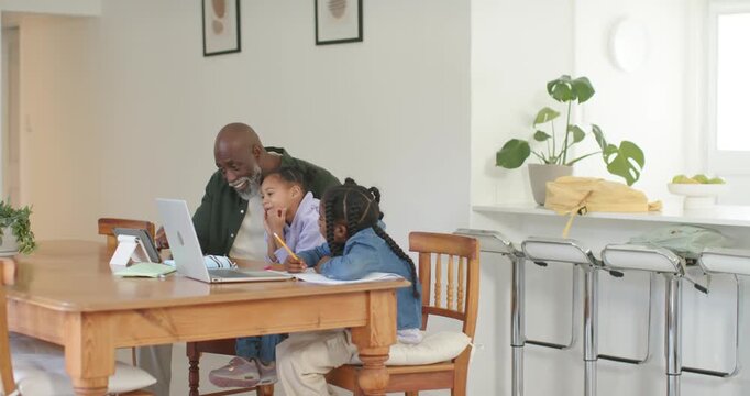 Mature man seeing homework on laptop guiding two kids with pencils leaning pointing typing at table
