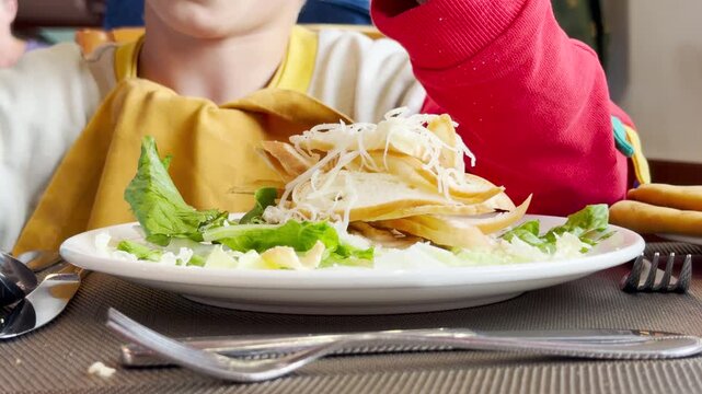 A young child eats a fresh salad on a cruise ship. He feels happy and hungry during the meal. The cozy dining room creates a joyful atmosphere.