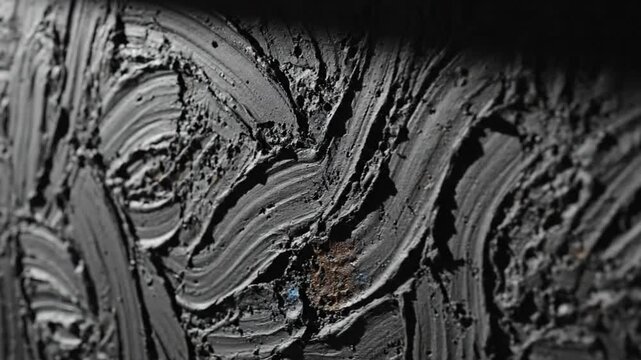 Abstract close up of textured dark grey painted surface with brushstroke patterns creating visual depth and shadows