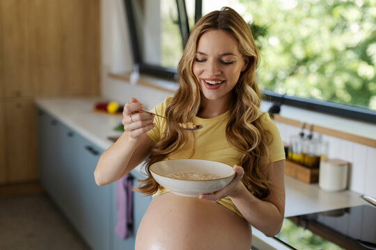 Happy mother-to-be eating wholesome porridge for breakfast while caring for her wellbeing and supporting healthy pregnancy
