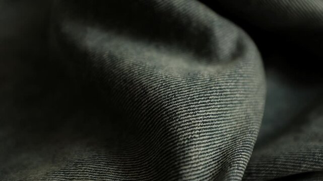 Close-up macro shot of detailed textured weave, folds, and soft twill lines of dark grey denim fabric. For stylish background, fashion presentations, textile manufacturing, clothing store commercials.