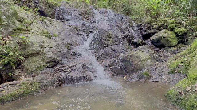 Kathu Dam waterfall water gently flowing down the rocks surrounded by lush green trees flowers and tables Patong on the Island of Phuket Thailand