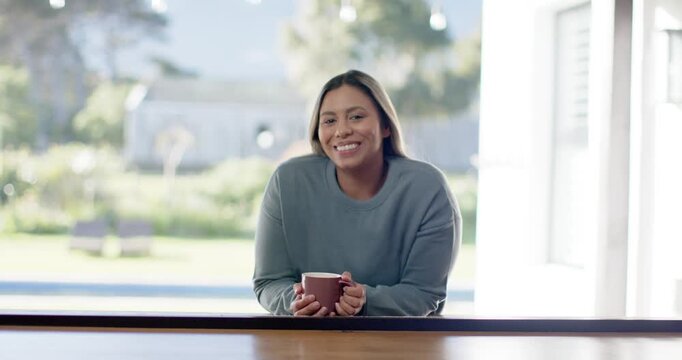 African American woman reacting to offscreen friend, leaning at home counter holding mug, laughing