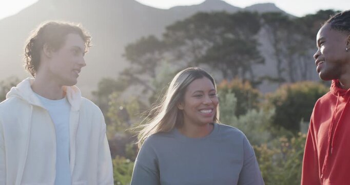 Diverse friends walking on foothill trail at golden hour, red hoodie man clapping, sharing joke