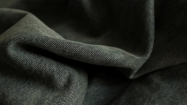Close-up macro shot of detailed textured weave, folds, and soft twill lines of dark grey denim fabric. For stylish background, fashion presentations, textile manufacturing, clothing store commercials.
