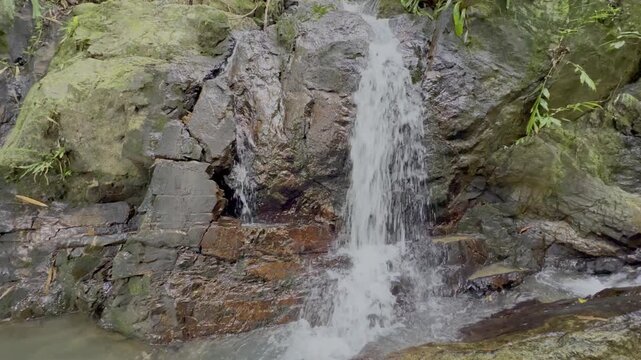 Kathu Dam waterfall water gently flowing down the rocks surrounded by lush green trees flowers and tables Patong on the Island of Phuket Thailand