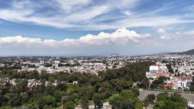 Aerial panoramic view of lush green trees and residential neighborhoods under dramatic clouds in Coyoacan, Mexico City, Mexico while the camera ascends