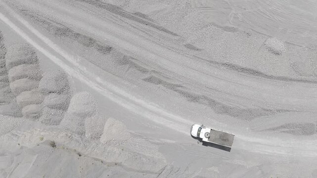 Top-down aerial view of a loaded dump truck driving along a dirt road between gravel piles in a sand and gravel quarry, D-Log M
