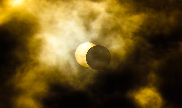 &Eacute;clipse solaire partielle voil&eacute;e par des nuages dor&eacute;s, la Lune masquant progressivement le Soleil