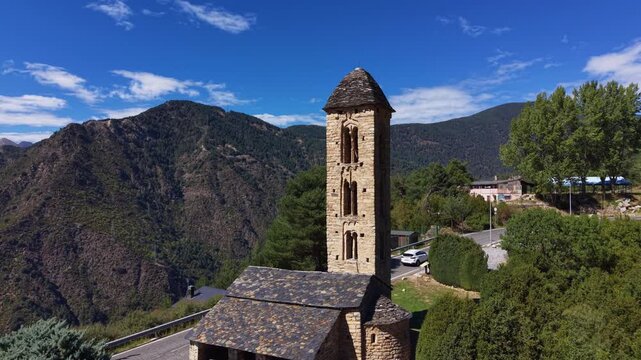 Sant Miquel d'Engolasters romanesque church with stone bell tower set among pine trees and Pyrenees mountains under blue sky in Andorra