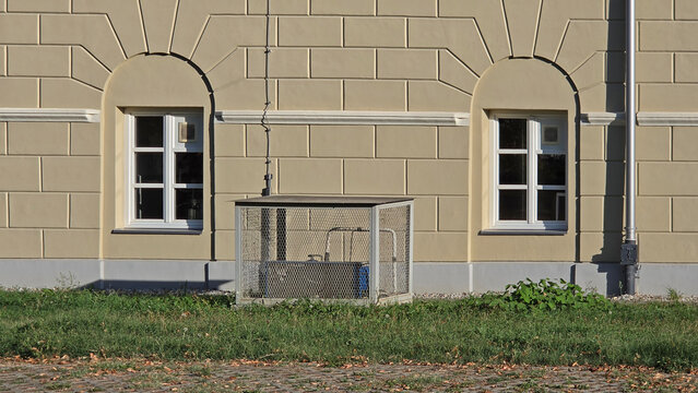 Beige classic building facade featuring arched windows with white mullions and utility cage on grass ground