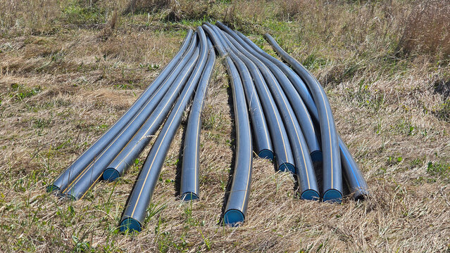 Black flexible plastic pipes with blue end caps resting on dry grass at an outdoor construction site