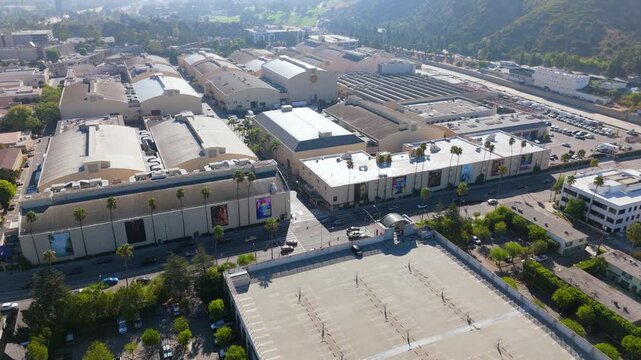 Cinematic aerial view of a movie studio lot in Burbank Los Angeles California. Film stages billboards palm trees and parking decks on a sunny summer day. Inspiring film industry district.