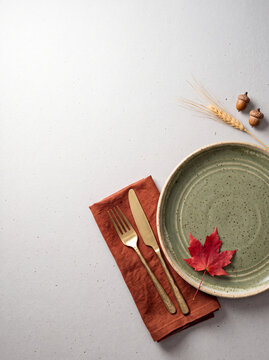 Thanks giving poster with text space, Autumnal Table Setting: A rustic ceramic plate with a single red maple leaf sits atop an earthy napkin, accompanied by golden cutlery, ready for a seasonal feast.