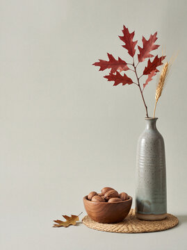 Thanks giving poster with text space, A ceramic vase holding a branch with red autumn leaves and a wheat stalk sits next to a wooden bowl filled with nuts, evoking the cozy essence of fall.