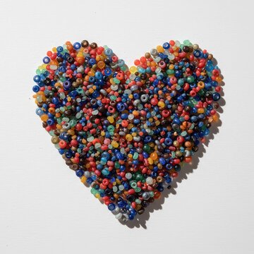 A vibrant heart shape carefully constructed using an assortment of small, multicolored glass beads, resting on a white surface ,shape ,pattern ,celebration