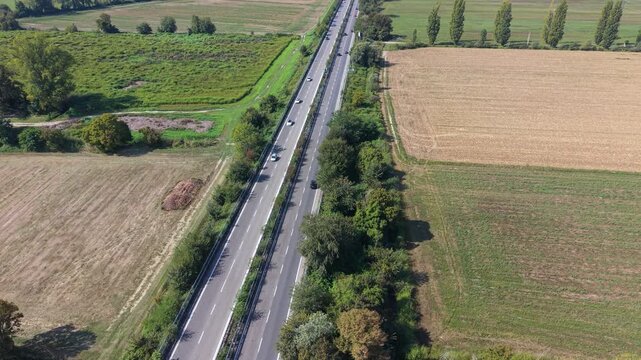 Aerial View of a Highway through Farmland: A high-angle shot captures a straight highway cutting through vast agricultural fields, with rows of crops and trees lining the roadside under a clear sky.