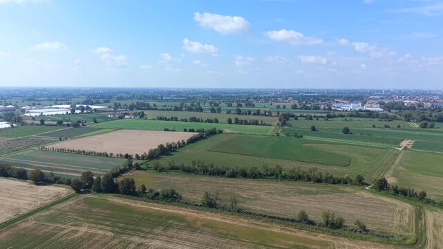 Vast Agricultural Landscape: An expansive aerial view showcases a patchwork of cultivated fields and green pastures under a bright, partly cloudy sky.