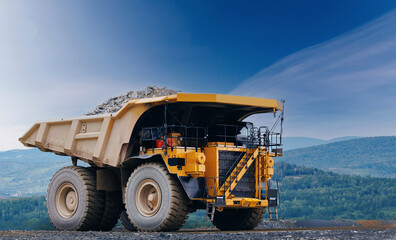 Closeup of massive yellow mining dump truck loaded with copper and gold ore against blue sky for industrial vehicle heavy equipment banner © Parilov