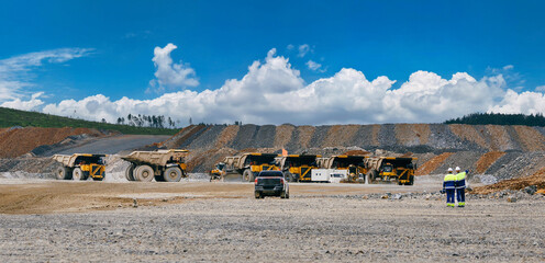 panorama view industry work of golden open pit mine with team workers and massive dump trucks and support vehicles at active quarry under blue sky for industrial © Parilov