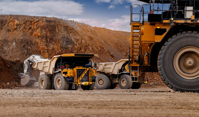 Plakat Quarry haul trucks parked at open gold pit edge with heavy wheels and rugged terrain for industrial transport background and logistics