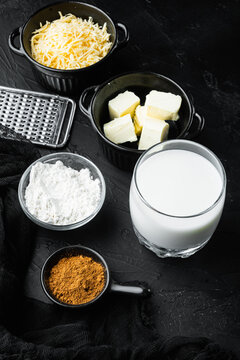 Bechamel sauce ingredients arranged on a dark textured stone surface including shredded cheese in a black ramekin, cubed butter in a small black bowl, powdered flour in a clear glass bowl