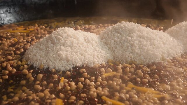 Adding rice to Uzbek wedding plov in a huge kazan over meat, carrots and chickpeas. Traditional outdoor cooking showcases national cuisine, festive customs and culinary tourism in Uzbekistan.