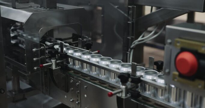 Empty metal cans enter processing machine along guided conveyor line. Automated equipment advances uniform containers toward next packaging operation in brewery