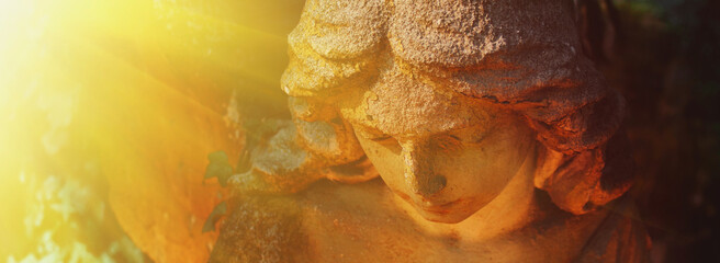 Fototapeta premium Ancient stone angel statue illuminated by radiant golden sunlight, symbolic image of heaven, divine light, faith, hope and eternal peace.