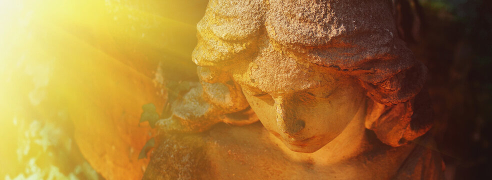 Ancient stone angel statue illuminated by radiant golden sunlight, symbolic image of heaven, divine light, faith, hope and eternal peace.