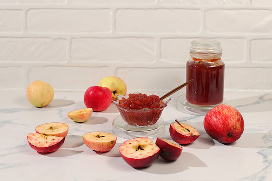 Fresh apple butter or jam made from red striped colored apple varieties. Jars of preserves, fruit butter, and fruit pur es arranged on a concrete kitchen countertop. Concept of homemade preserves,