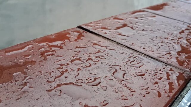 Rain droplets falling on textured red ceramic bricks