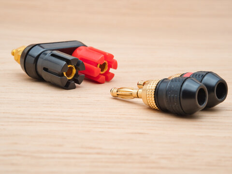 Audio Connectors and Banana Plugs - Close-up of a speaker binding post terminal with red and black banana plugs on a light wooden background, showing audio connection component