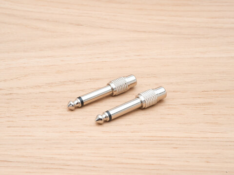 Two Silver Audio Jack Connectors - Two silver audio jack connectors, also known as phone plugs or TS connectors, are arranged diagonally on a light wood grain background.