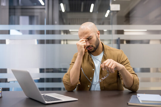Burnout and workplace stress, tired businessman working on laptop at office desk feeling headache and eye strain during a long day of financial analysis