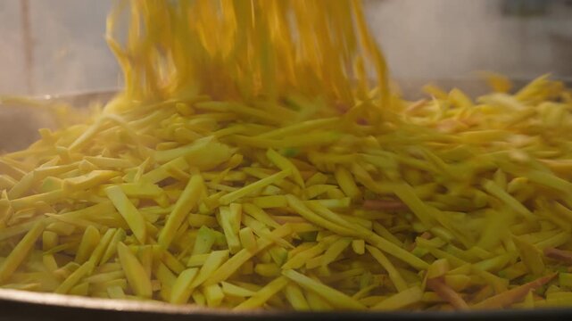 Yellow carrots are added to Uzbek wedding plov cooking in a huge kazan. Traditional outdoor food preparation showcases Uzbekistan's national cuisine, festive customs and culinary tourism