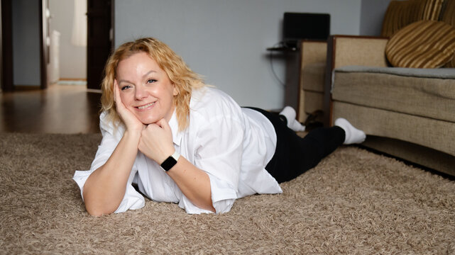Woman relaxing on carpet in living room while smiling and posing for the camera