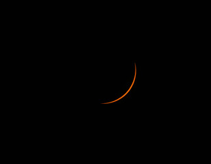 A thin orange crescent moon glows against a pitch black sky. © Kit Leong