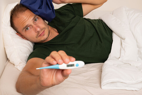 Sick Man Checking His Temperature with Digital Thermometer in Bed