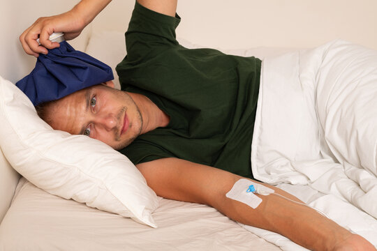 Sick Man with IV Cannula and Cold Compress Resting in Bed