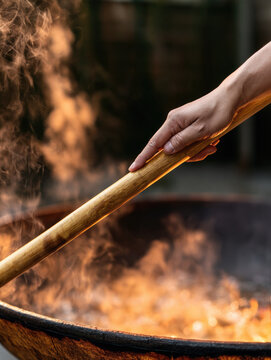 Bamboo stirring pole adult hand outdoor fire boiling water iron pan steam rising over rustic wood fire while relaxed adult hand steadies carved bamboo pole above glowing flames, with warm light