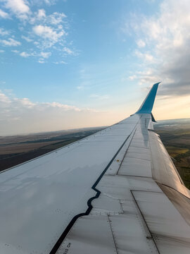 Passenger plane airplane wing view from a window flying low above rural ground fields and town landscape. Beautiful clear sunset soft sky background template with light clouds at golden hour. Freedom.