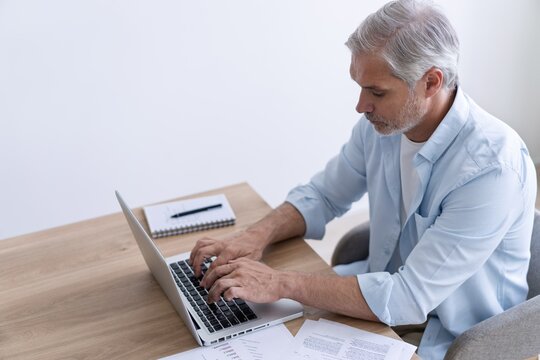 Portrait of happy 40s freelancer man sitting at desk with laptop computer at home office