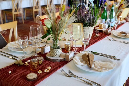 Wedding table setting with rustic decor, white tablecloth, terracotta runner, and wheat centerpieces.