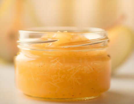 Fresh sweet pear jam inside a small glass jar on a bright kitchen table with ripe yellow fruits in soft warm light for breakfast concept close shot homemade transparent placed surface
