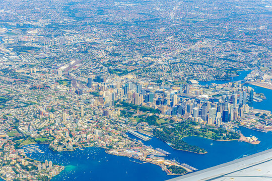 View through plane window and over wing while flying into Sydney with business district and sprawling urban area.
