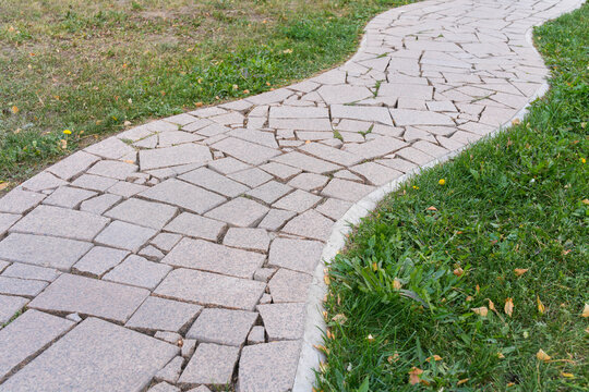 Winding stone flagstone pathway through green lawn in public park. Garden landscape design. Real Photo