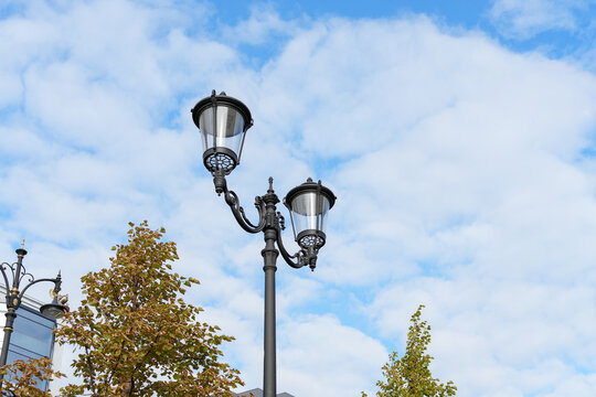 Classic black double street lamp post against cloudy blue sky. Urban lighting and architecture concept. Real Photo
